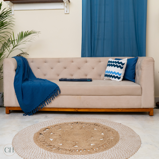 CustHum - Upholstered sofa in beige with hand-tufting against blue curtain and with blue cushions and throw (front view)