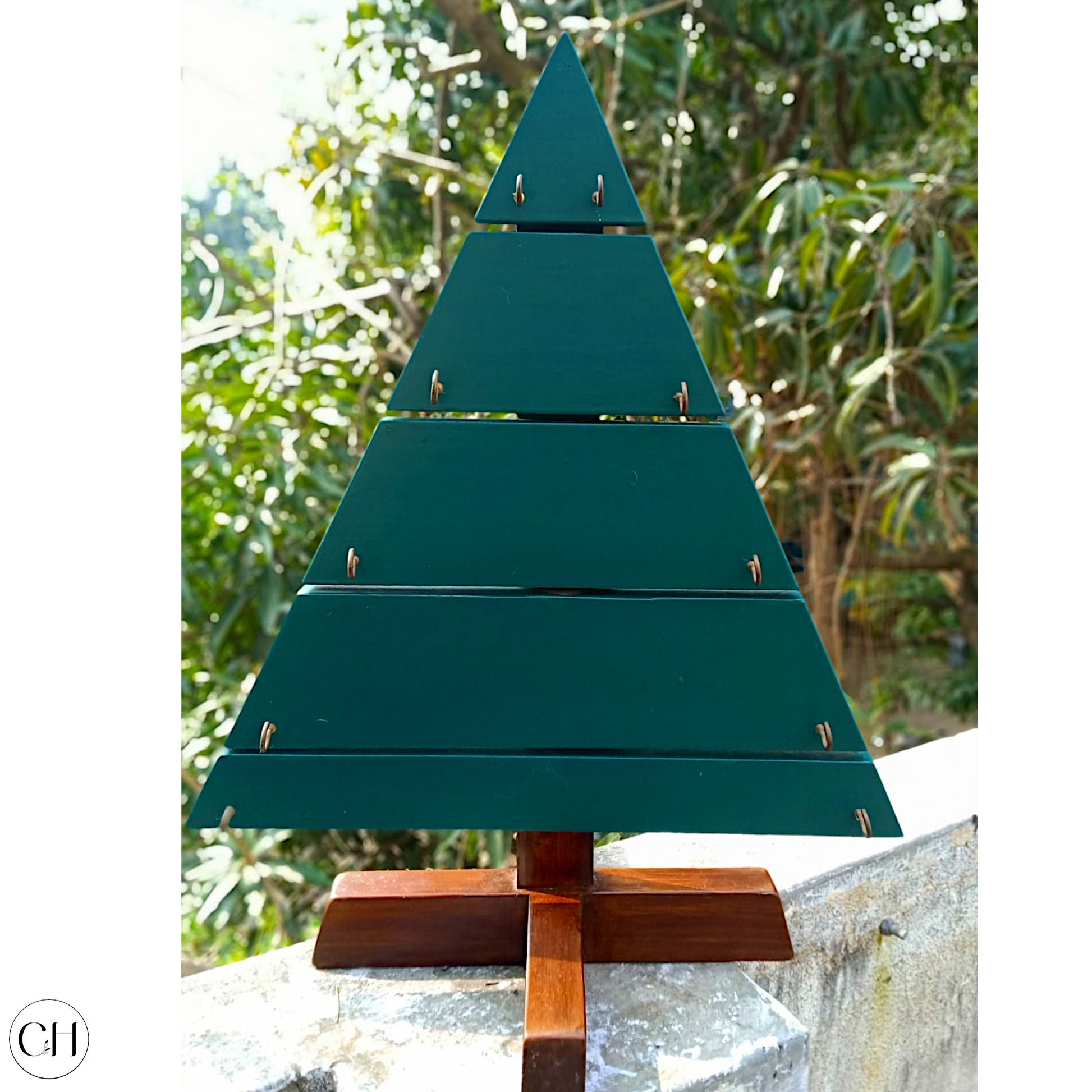 CustHum Noel-small wooden christmas tree with hooks to hang ornaments, placed against a background of greenery